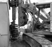 Drilling caissons against an existing structure to support shoring for a new lower level garage and room addition.
