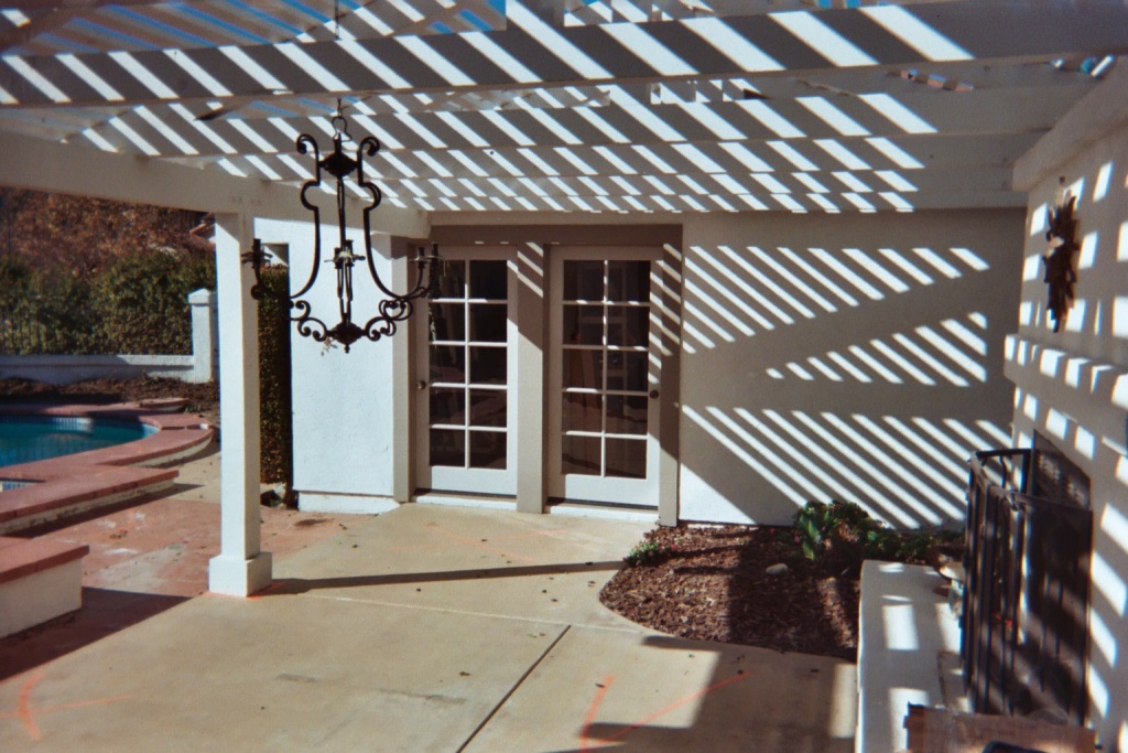 This single image shows the original patio, pool with raised red cast-in-place coping, and the original wrought iron fence and columns beyond (see the waterfeature image above).